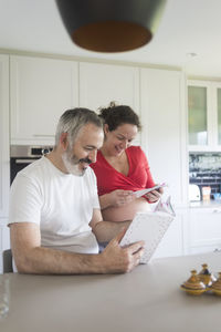 Man and pregnant woman reading book at kitchen