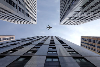 Big airplane flying high above modern city skyscrapers with many windows in business cluster