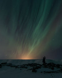 Rear view of silhouette man standing against aurora borealis at night during winter