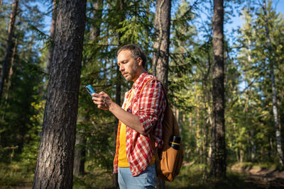 Rear view of young woman photographing while standing in forest