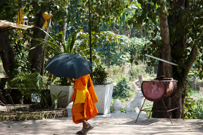 Monk holding umbrella while walking on road