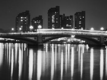 Illuminated bridge over river by buildings against sky at night