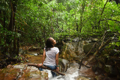 Rear view of woman sitting by waterfall in forest