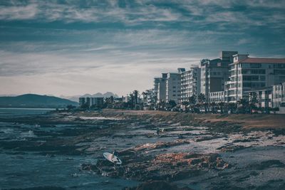 View of city at waterfront against cloudy sky