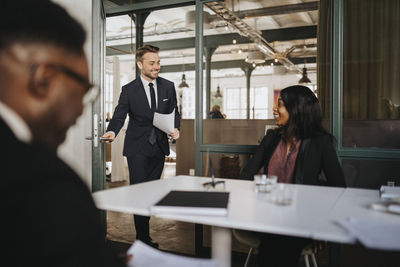 Smiling businessman looking at female entrepreneur while entering in board room at office