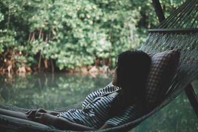 Thoughtful woman relaxing in hammock against lake