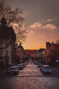 Cars parked on street by buildings against sky during sunset