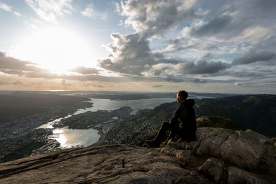 Man sitting on rock against sky