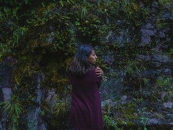 Side view of young woman standing in forest