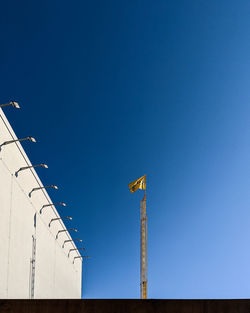 Low angle view of crane by building against clear blue sky