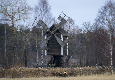 Traditional windmill by birds on field against bare trees