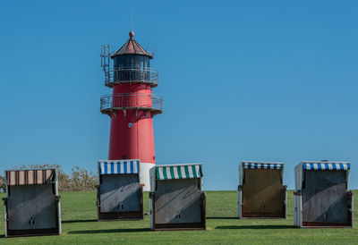 Lighthouse and hooded beach chairs against clear blue sky