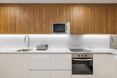 Stylish kitchen with modern furniture in white color with wooden cupboards for kitchenware.