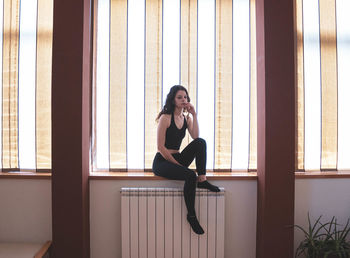 Portrait of young woman sitting on window at home