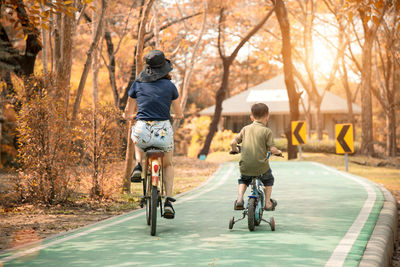 Rear view of mother and son riding bicycles on road amidst trees