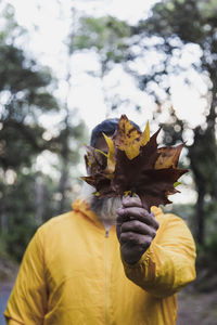 Man holding autumn leaf in front face person