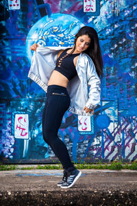 Full length of smiling young woman standing against graffiti wall