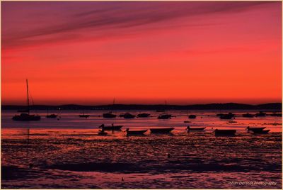 Silhouette boats moored on sea against orange sky