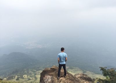 Rear view of young man standing on mountain during foggy weather