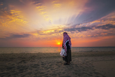 Rear view of woman on beach against sky during sunset