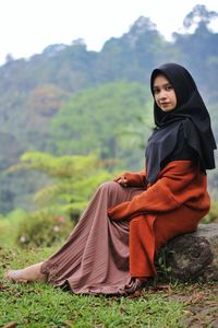 Young woman sitting on land against trees