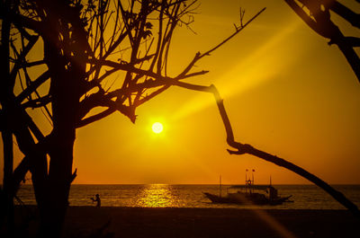 Silhouette tree by sea against orange sky during sunset