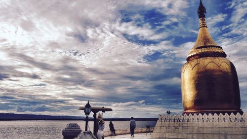 Golden stupa by river against cloudy sky