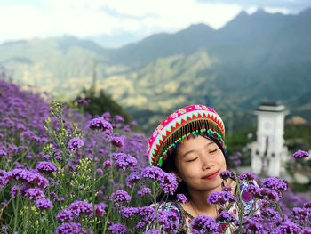 Close-up of young woman by purple flowers against mountain