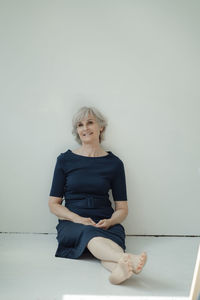 Happy senior businesswoman sitting in front of wall