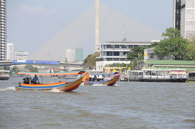 Boats in river by buildings against sky