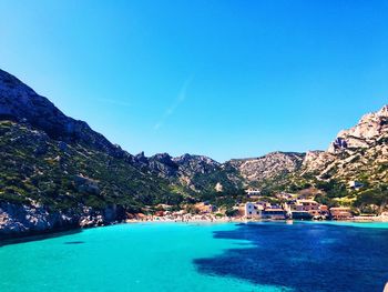 Scenic view of sea and mountains against clear blue sky