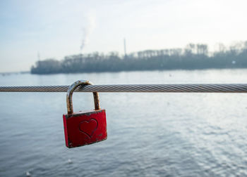 Close-up of love padlock hanging on rope by sea against sky