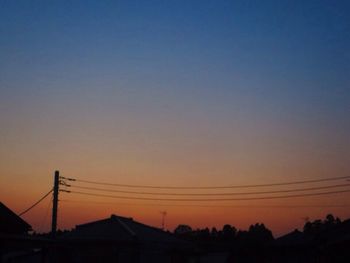 Silhouette electricity pylons against clear sky during sunset