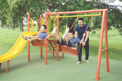 Father with sons enjoying swings at park