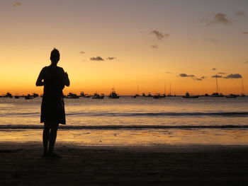 Full length rear view of woman standing on beach during sunset