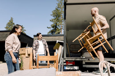 Couple looking at mover unloading chairs from truck on sunny day