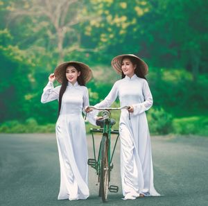 Women wearing white clothing and asian style conical hats while walking with bicycle on road