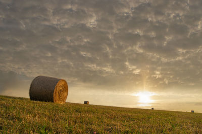 Hay bales on field against sky during sunset