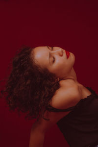 Side view of young woman with eyes closed sitting against red background