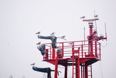 Low angle view of seagulls perching on radar tower against clear sky