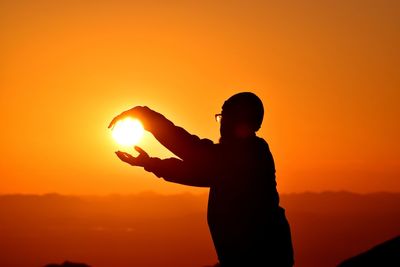 Silhouette man holding orange against sky during sunset