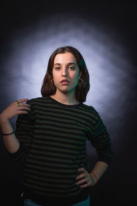 Portrait of young woman standing against black background