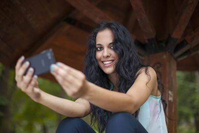 Low angle view of cheerful young woman using phone while sitting in gazebo