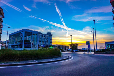 Road by buildings against blue sky during sunset