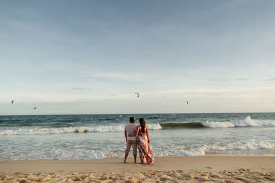 Rear view of couple standing on beach against sky