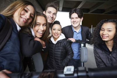 Portrait of smiling male and female teenage friends with electric push scooters below bridge