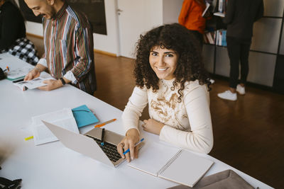 Portrait of smiling young woman with curly hair studying at community college