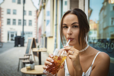 Portrait of young woman drinking ice tea from glass at restaurant