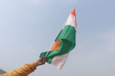 Low angle view of hand holding flag against sky