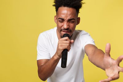 Young man using mobile phone while standing against yellow background